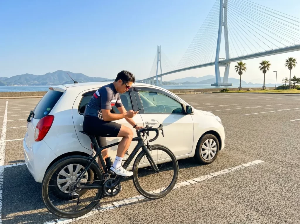 海沿いの駐車場で車とロードバイクを確認する日本人男性